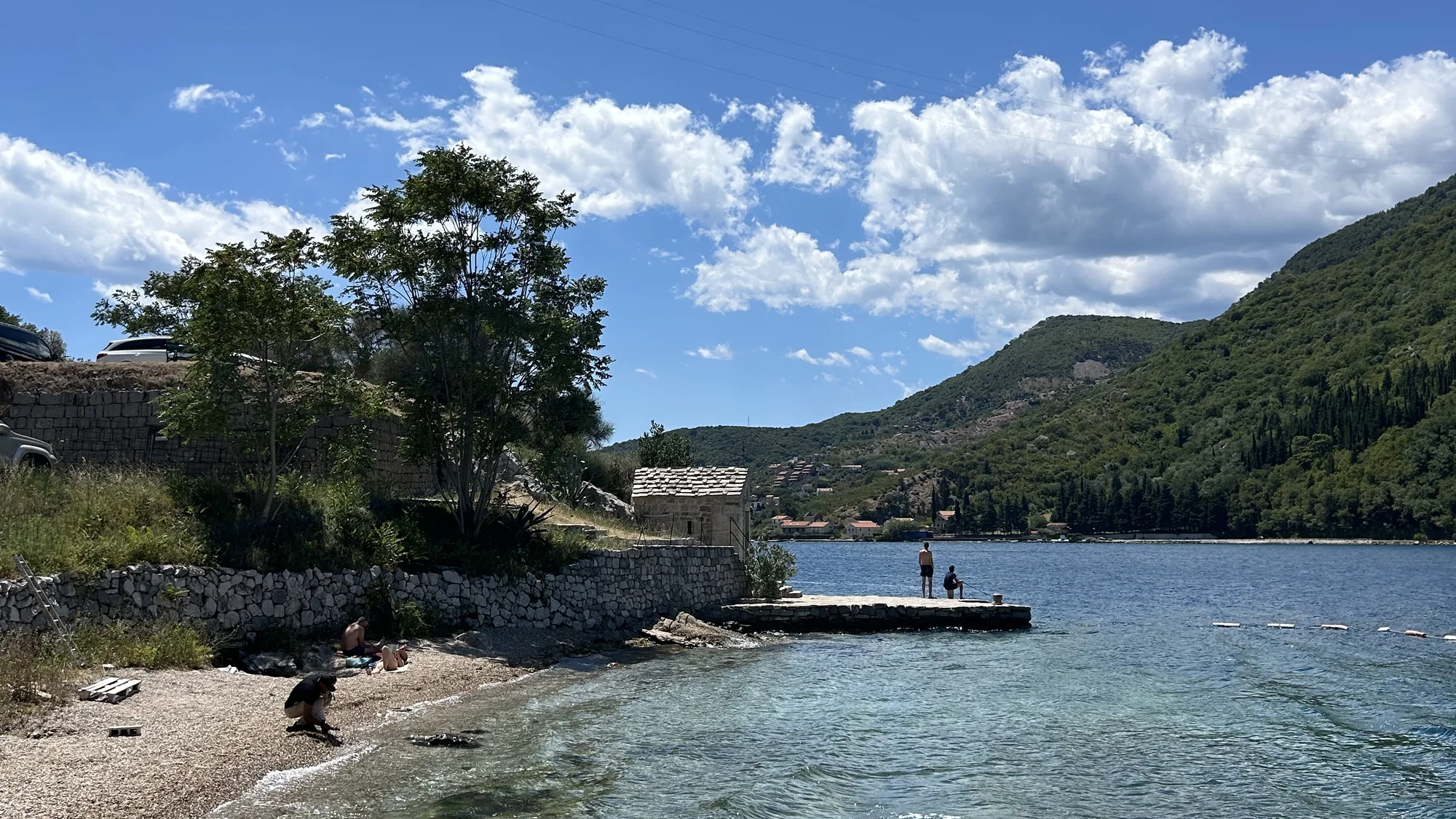 Une baie à l'eau claire, une petite jetée et des collines boisées